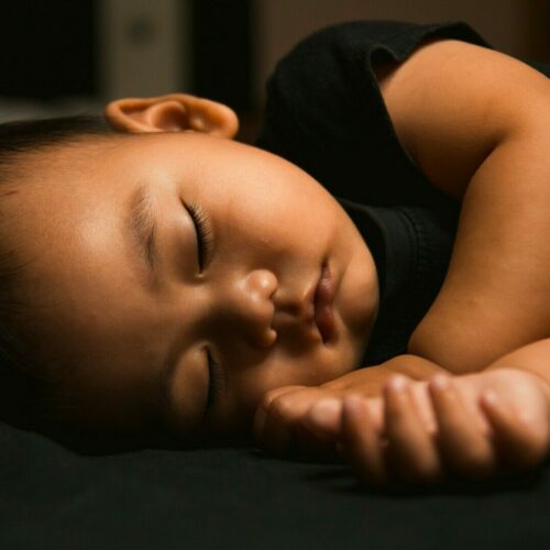 baby in black tank top lying on black textile
