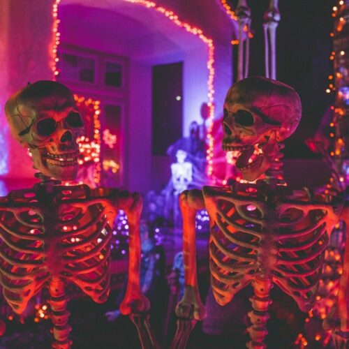 two skeleton near white concrete building with string lights at daytime